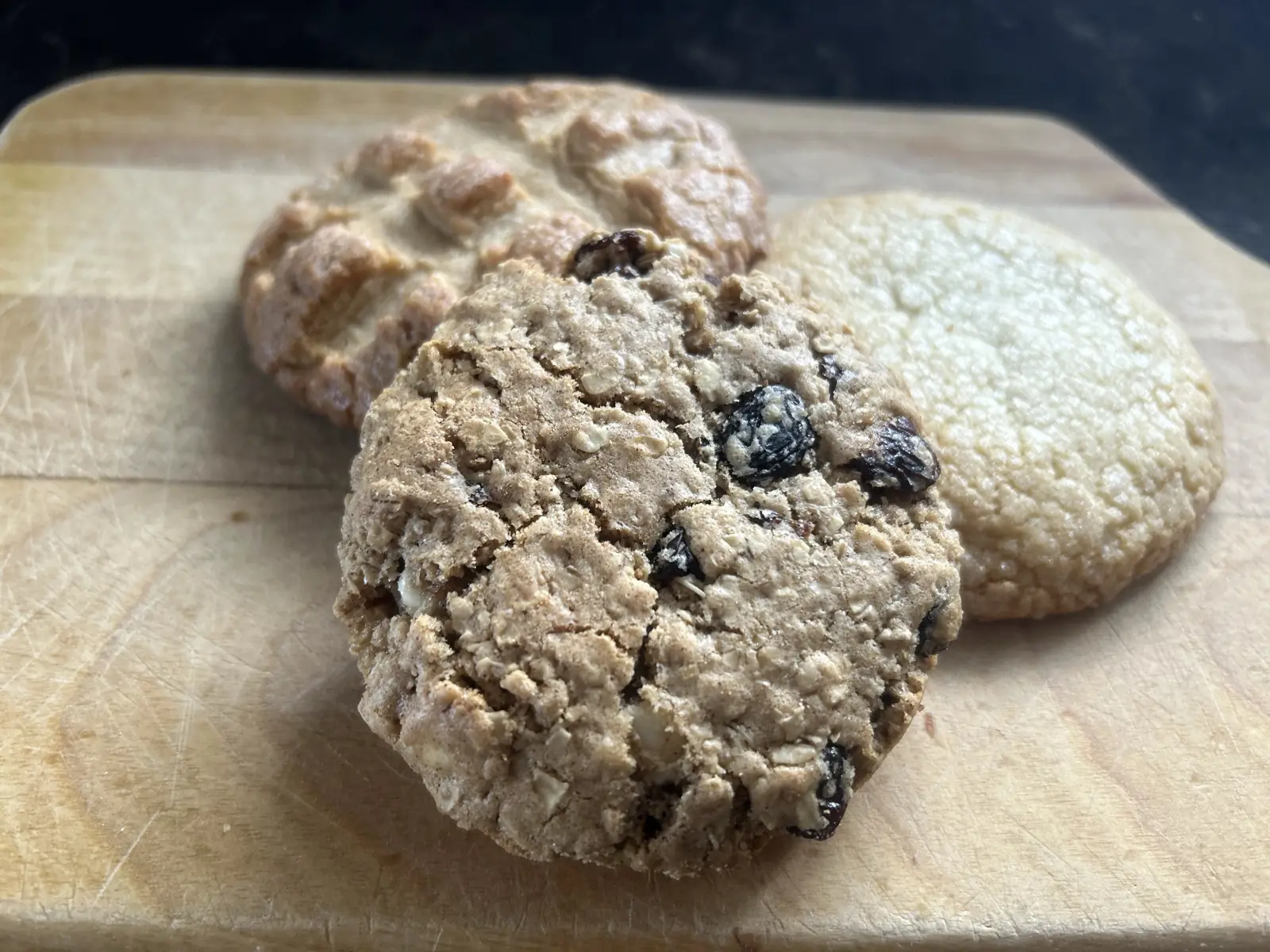 Three bear-sized cookies on a wooden board: peanut butter, oatmeal raisin and sugar