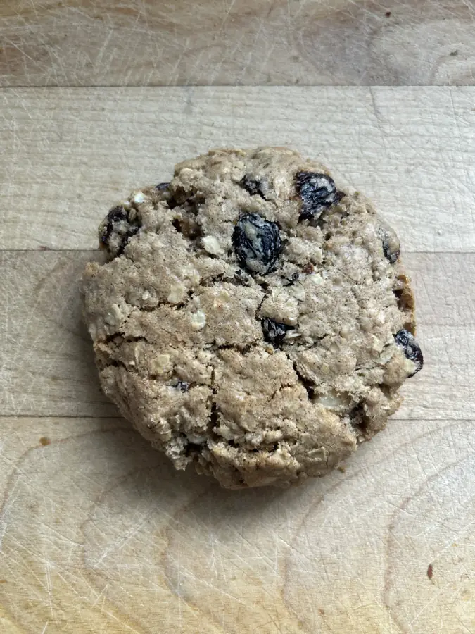 A hearty oatmeal raisin cookie packed with oats, plump raisins and white chocolate chips on a wooden board