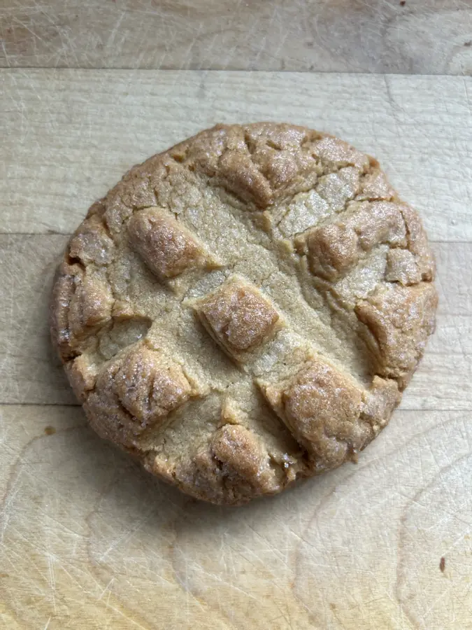 A peanut butter cookie with the classic criss-cross fork top on a wooden board