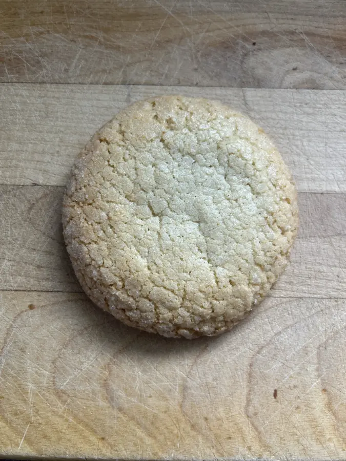 A big golden sugar cookie with a crackled, sugar-crusted top on a wooden board